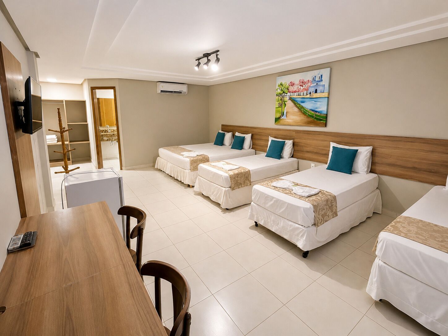 A hotel room with three beds, a wooden desk, a chair, a TV, and an air conditioning unit.