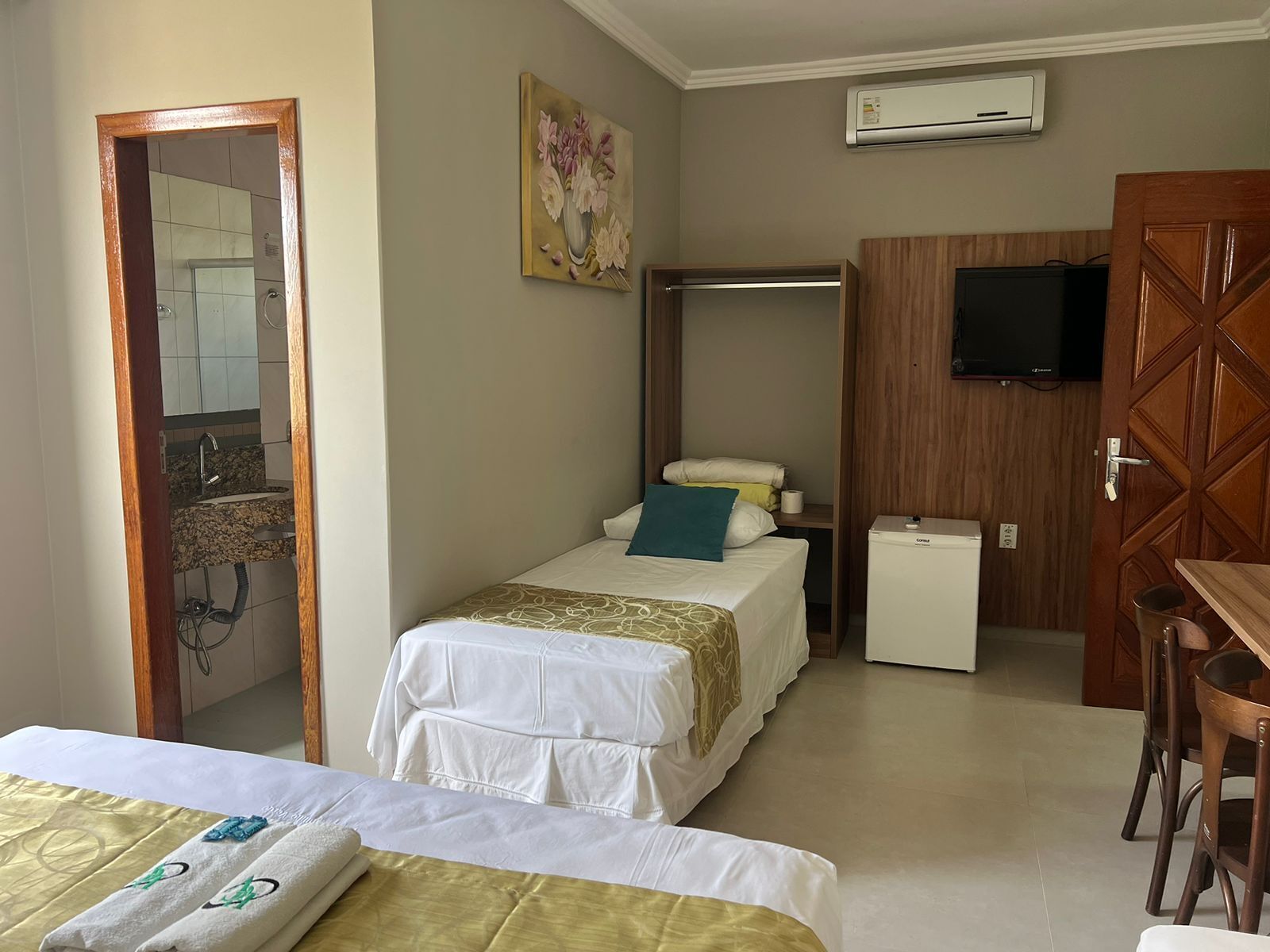 A hotel room with two beds, a small kitchenette, a TV, and an air conditioning unit.