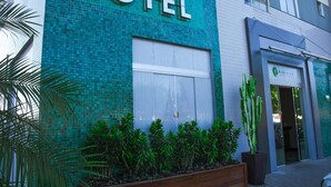 A hotel with a prominent "HOTEL" sign, a large glass door entrance, and a small garden area with plants. - Pioneiro Hotel (Teixeira de Freitas)