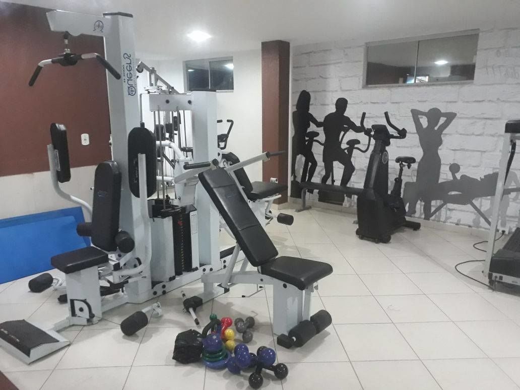 Une salle de sport équipée de divers appareils d’exercice, notamment un banc de développé couché, des haltères et des appareils de cardio.