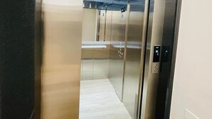 An elevator with metallic walls and a reflective floor, featuring a control panel with directional arrows. - Pioneiro Hotel (Teixeira de Freitas)