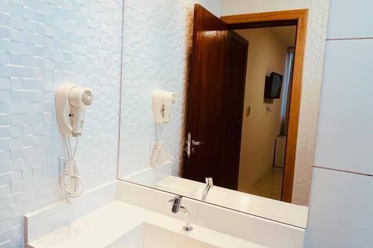 A bathroom with a white sink, a mirror, and a towel dispenser.