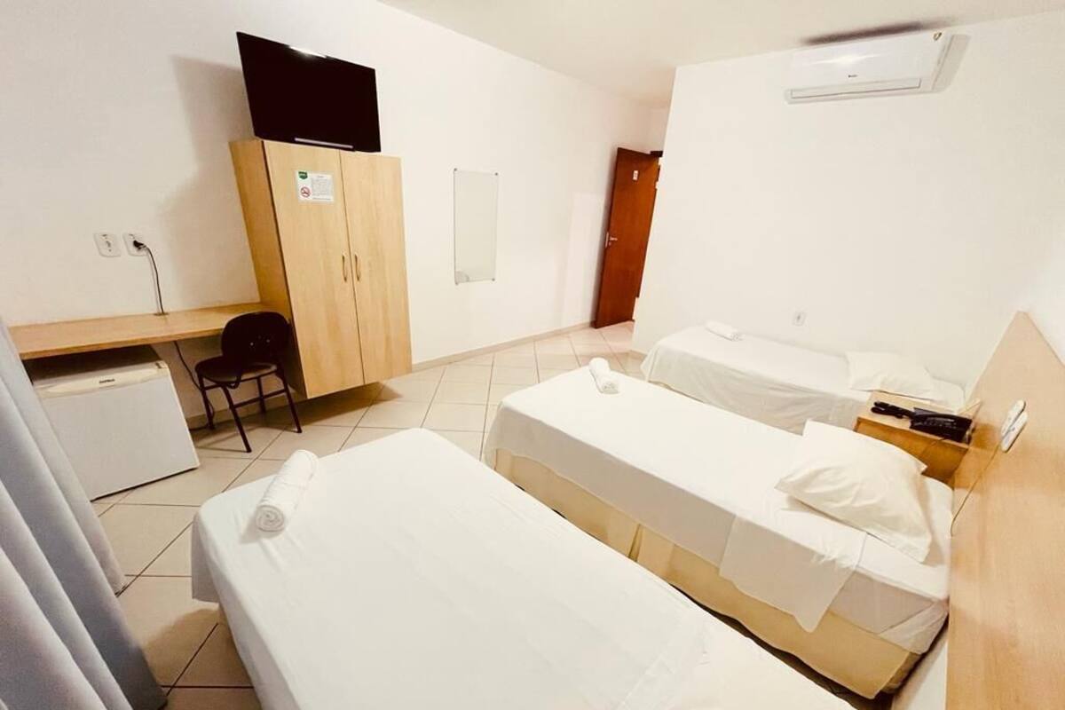 A room with two single beds, a desk, a chair, a wardrobe, and a television.