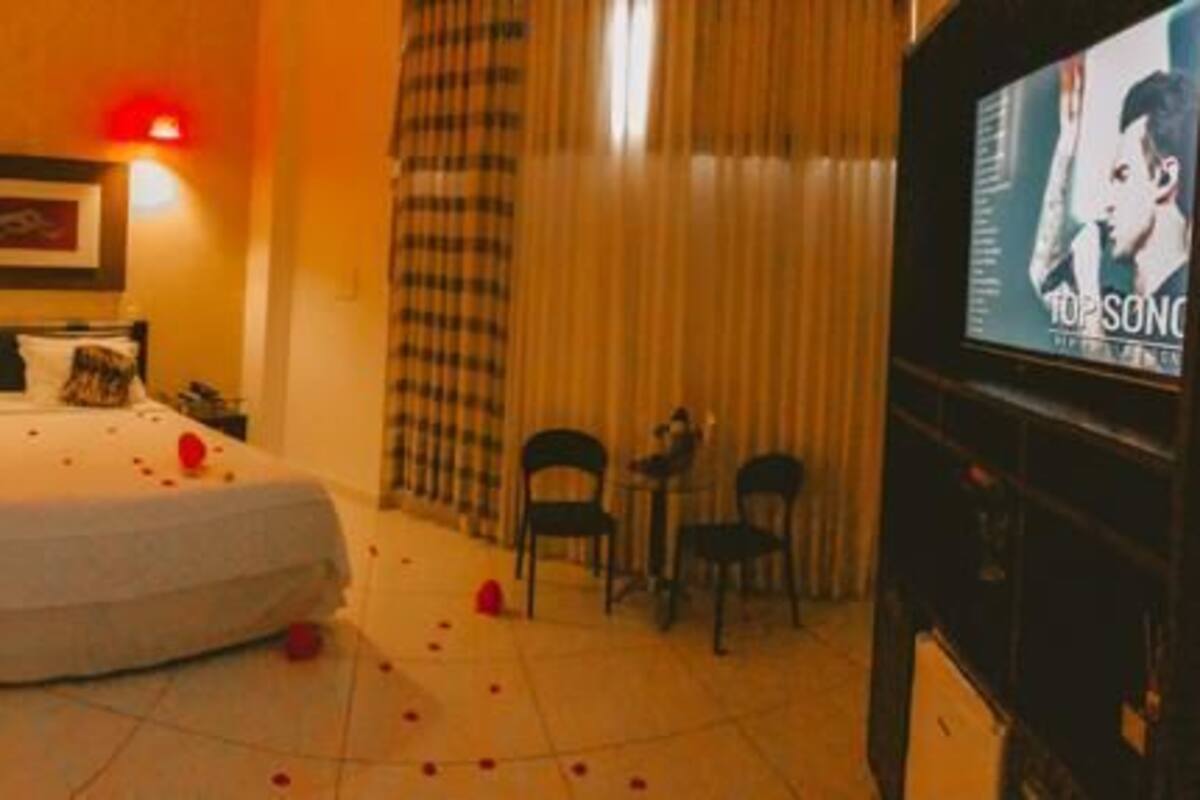 A hotel room with a bed, a TV, a mirror, and a door.