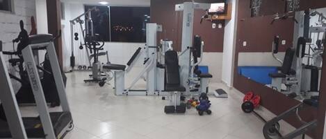 A gym with various exercise machines, a treadmill, and weights.