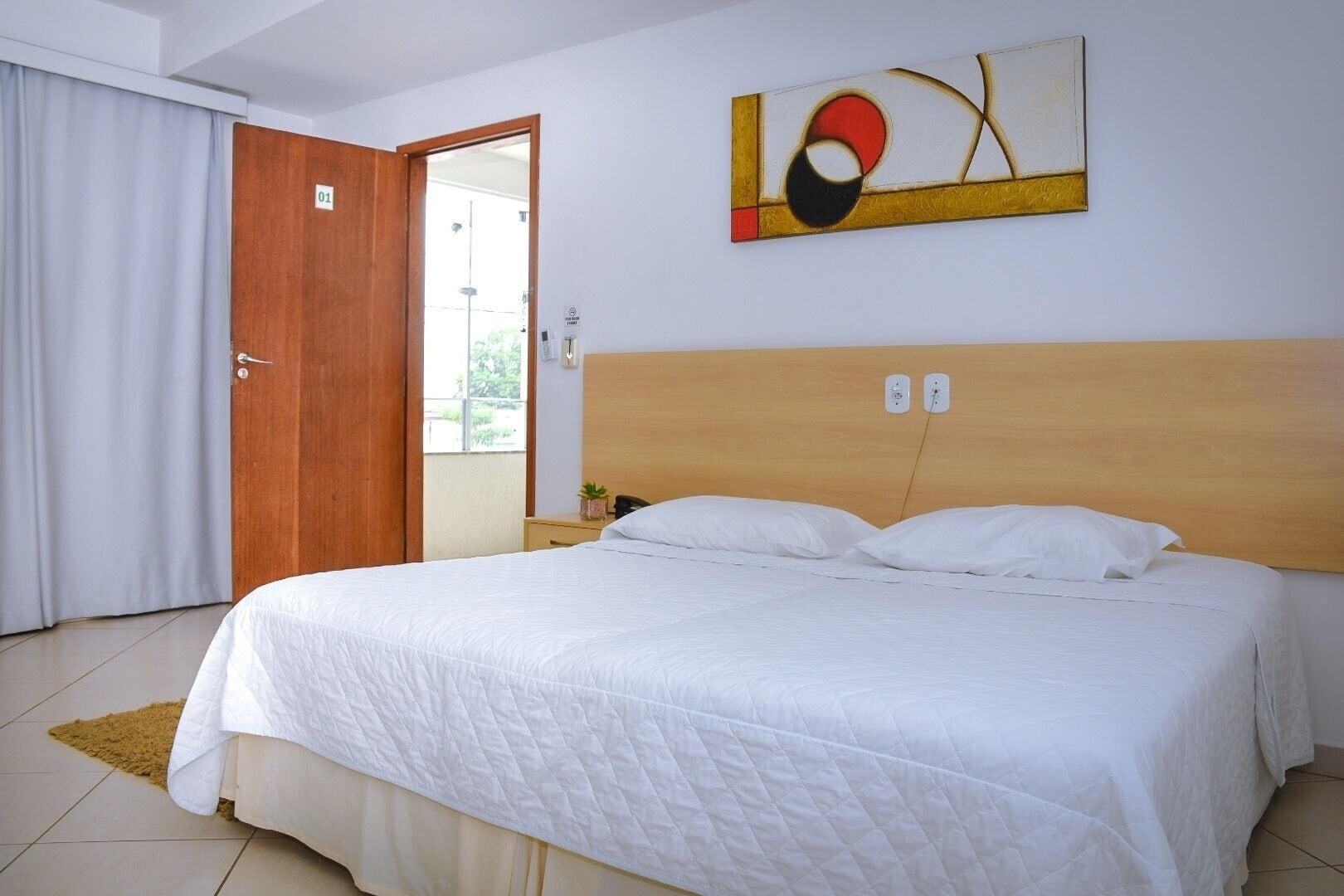 A hotel room with a large bed, a wooden headboard, a painting on the wall, and a door leading to a balcony.
