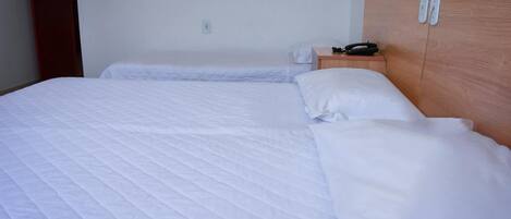 A hotel room with a large bed, a wooden headboard, a bedside table with a phone, and a wall socket.