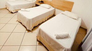 A hotel room with three single beds, a wooden headboard, a bedside table with a lamp, and an air conditioning unit on the wall. - Pioneiro Hotel (Teixeira de Freitas)