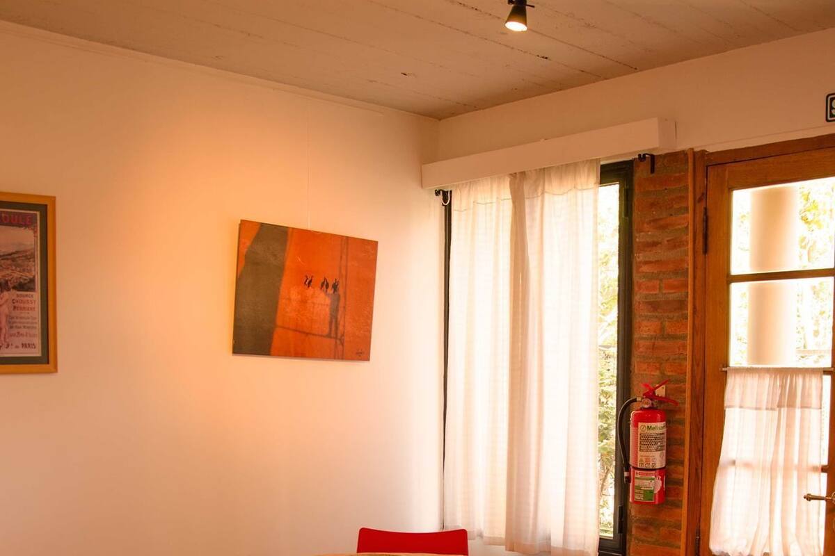 A dining area with a round table, four red chairs, a bowl on the table, and a painting on the wall.