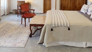 Une chambre à coucher avec un lit, une armoire en bois, un fauteuil rouge, une petite table avec une lampe et un lustre.