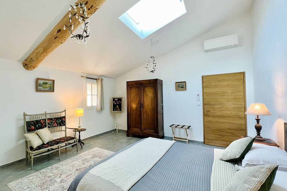 Une chambre à coucher avec un lit, une armoire en bois, une petite table avec une lampe, un banc et une lucarne.