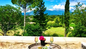 Un espace extérieur rustique aménagé avec une table en fût de bois, deux tabourets en bois et une vue sur un paysage luxuriant.