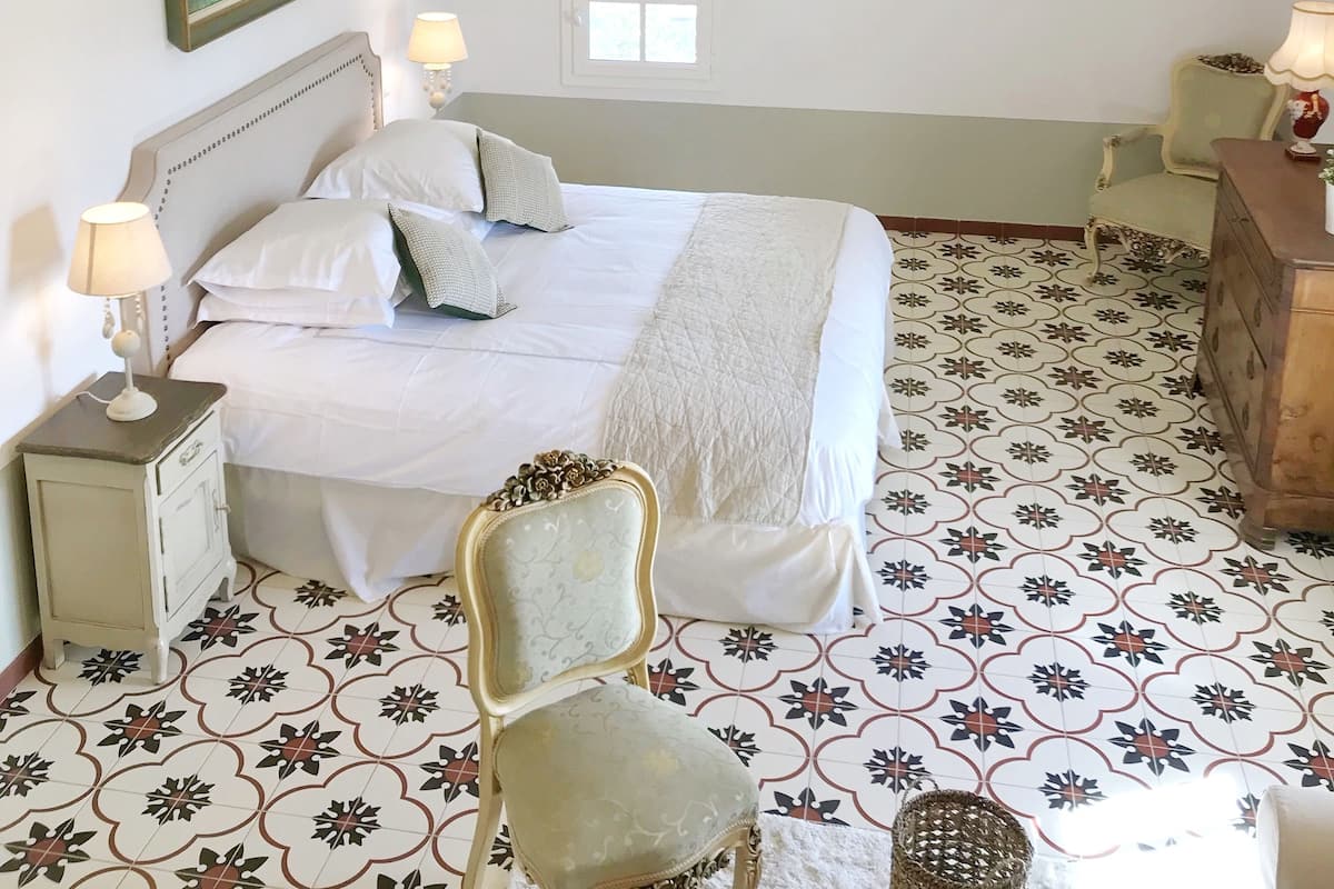 Une chambre à coucher avec un grand lit, un lustre, une chaise, une commode et une fenêtre.