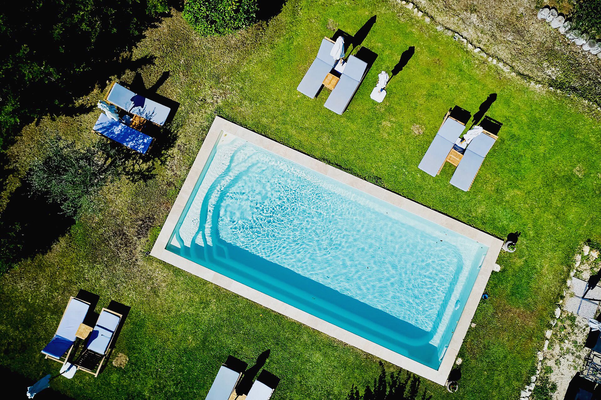 An aerial view of a rectangular swimming pool surrounded by a well-maintained lawn with several lounge chairs and umbrellas.