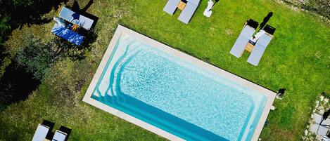 An aerial view of a rectangular swimming pool surrounded by a well-maintained lawn with several lounge chairs and umbrellas.
