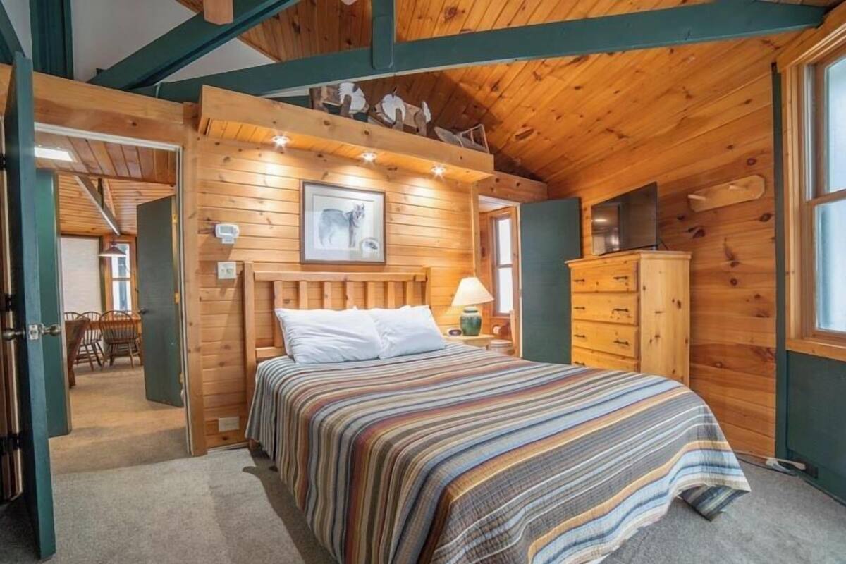 A wooden cabin bedroom with a bed, a dresser, a television, and a framed picture on the wall.