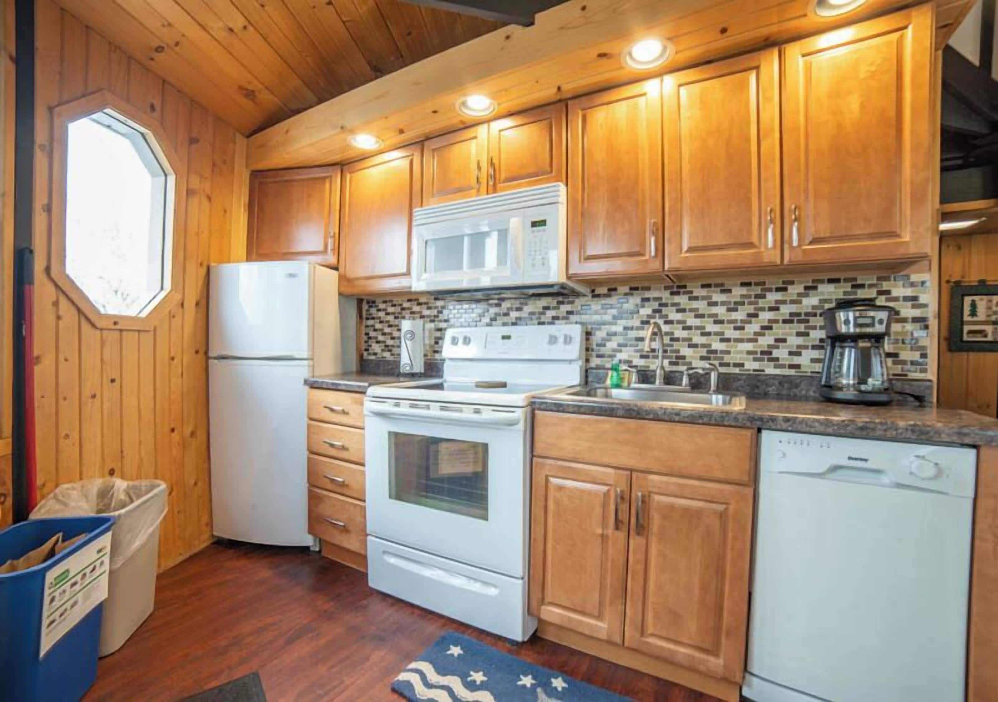 A kitchen with wooden cabinets, a microwave, a stove, a dishwasher, and a window with a view.
