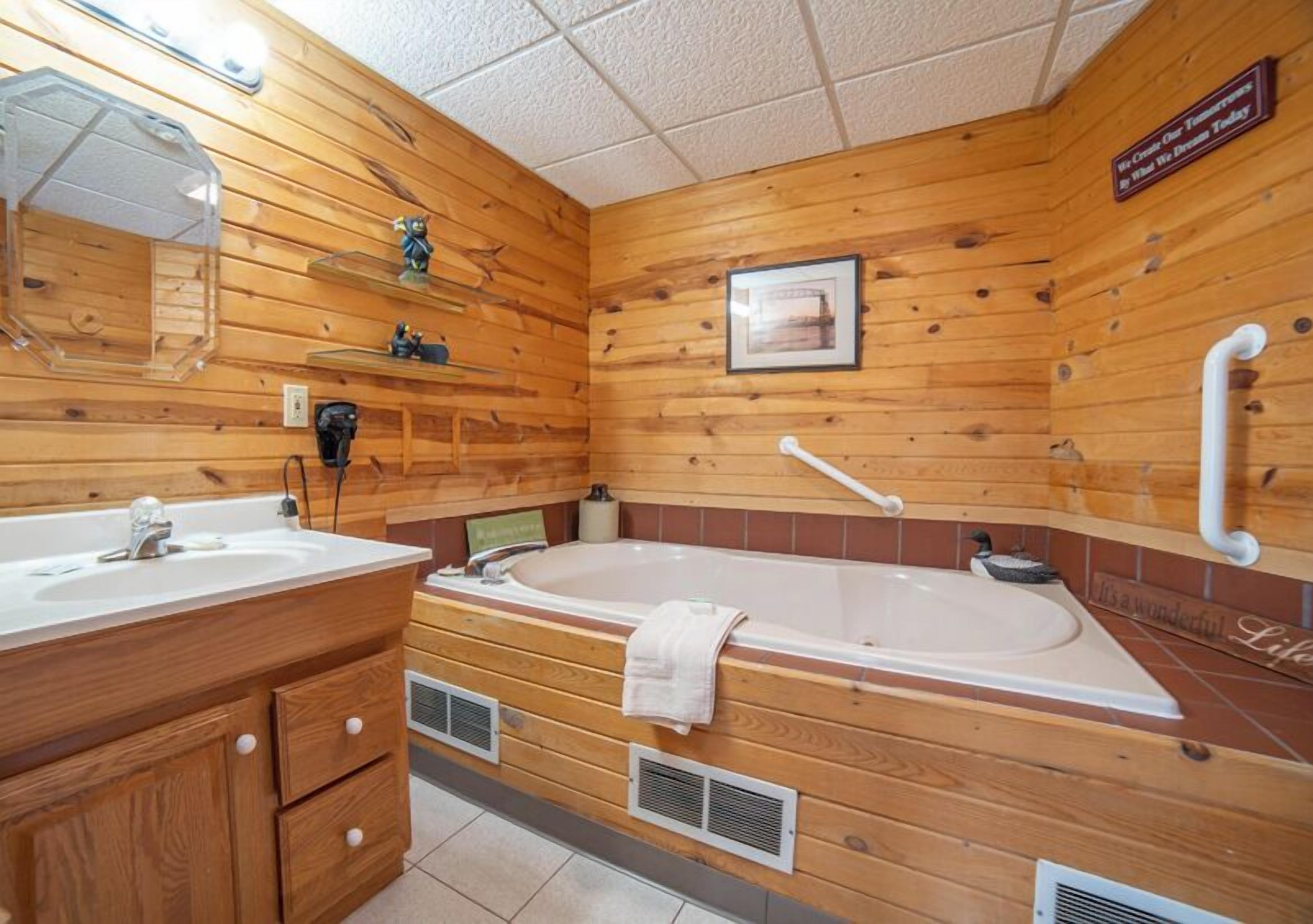 Un baño de estilo cabaña con una bañera grande, un tocador con espejo y un estante con artículos de aseo.