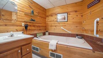Un baño de estilo cabaña con una bañera grande, un tocador con espejo y un estante con artículos de aseo.