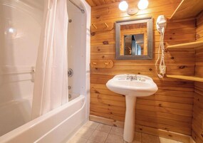 Baño de cabaña de madera con bañera, lavamanos y espejo.