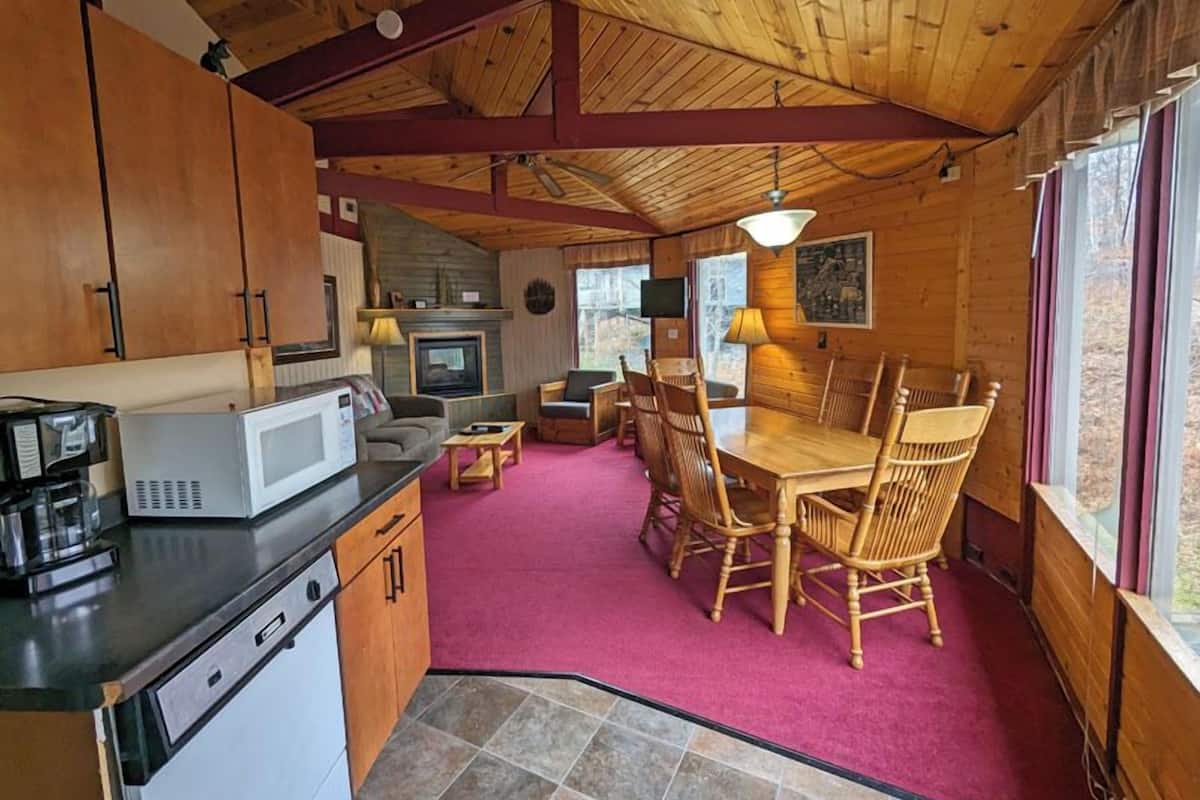 A cozy cabin-style kitchen with wooden cabinets, a microwave, and a dining area with a table and chairs.