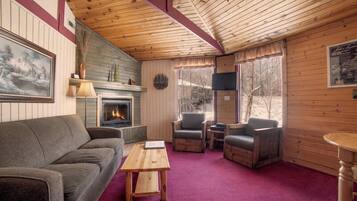 A cozy cabin interior with a fireplace, wooden furniture, and a view of the outdoors.