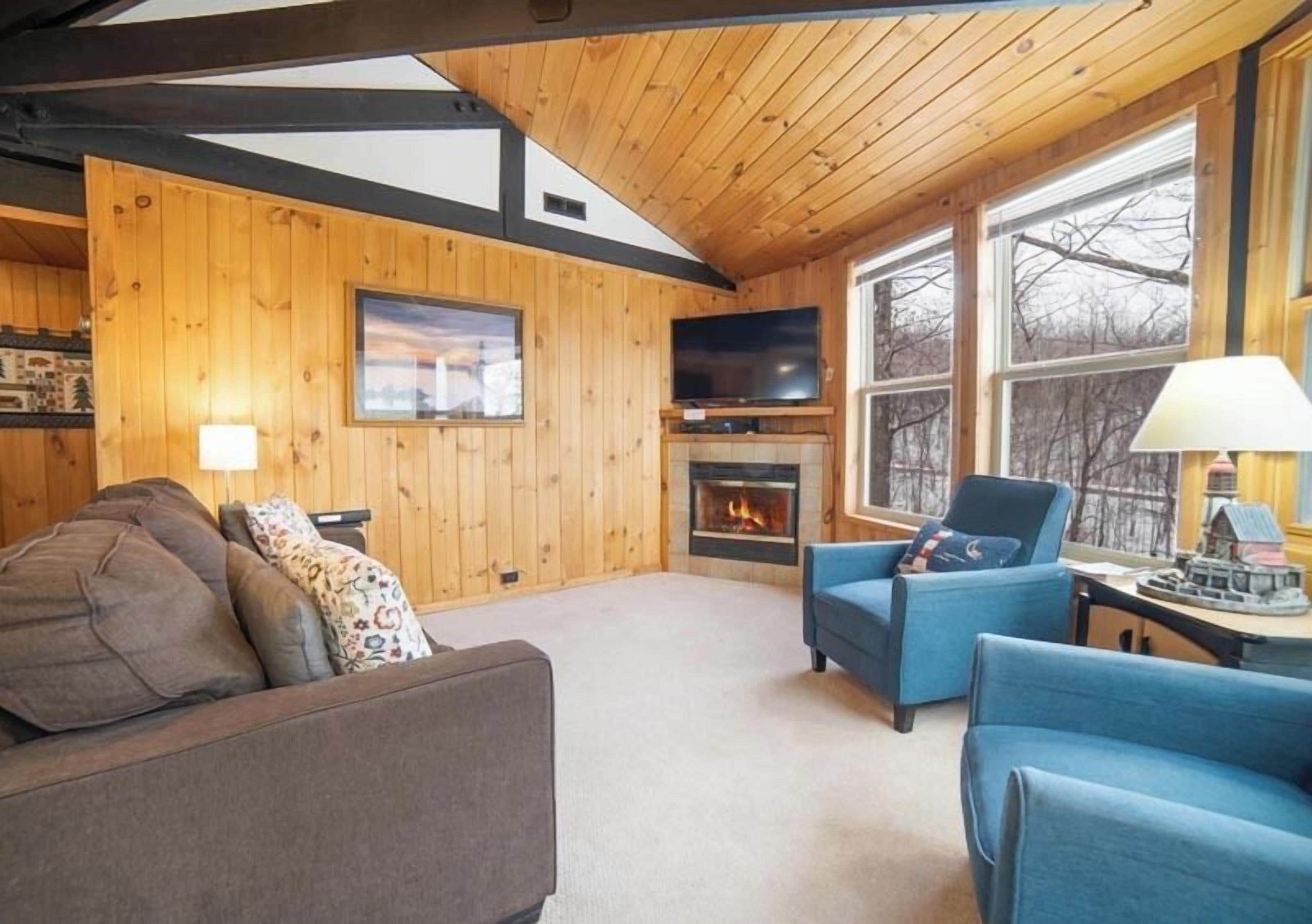 Un salon chaleureux avec des murs en bois, une cheminée, un téléviseur et des fauteuils confortables.