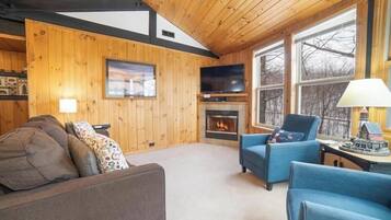 Un salon chaleureux avec des murs en bois, une cheminée, un téléviseur et des fauteuils confortables.