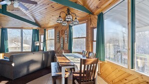 L'interno accogliente di un rifugio con soffitto in legno, ampie finestre, un tavolo da pranzo e un divano.