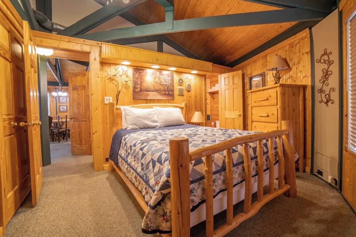 A cozy wooden cabin bedroom with a bed, a dresser, and a nightstand.