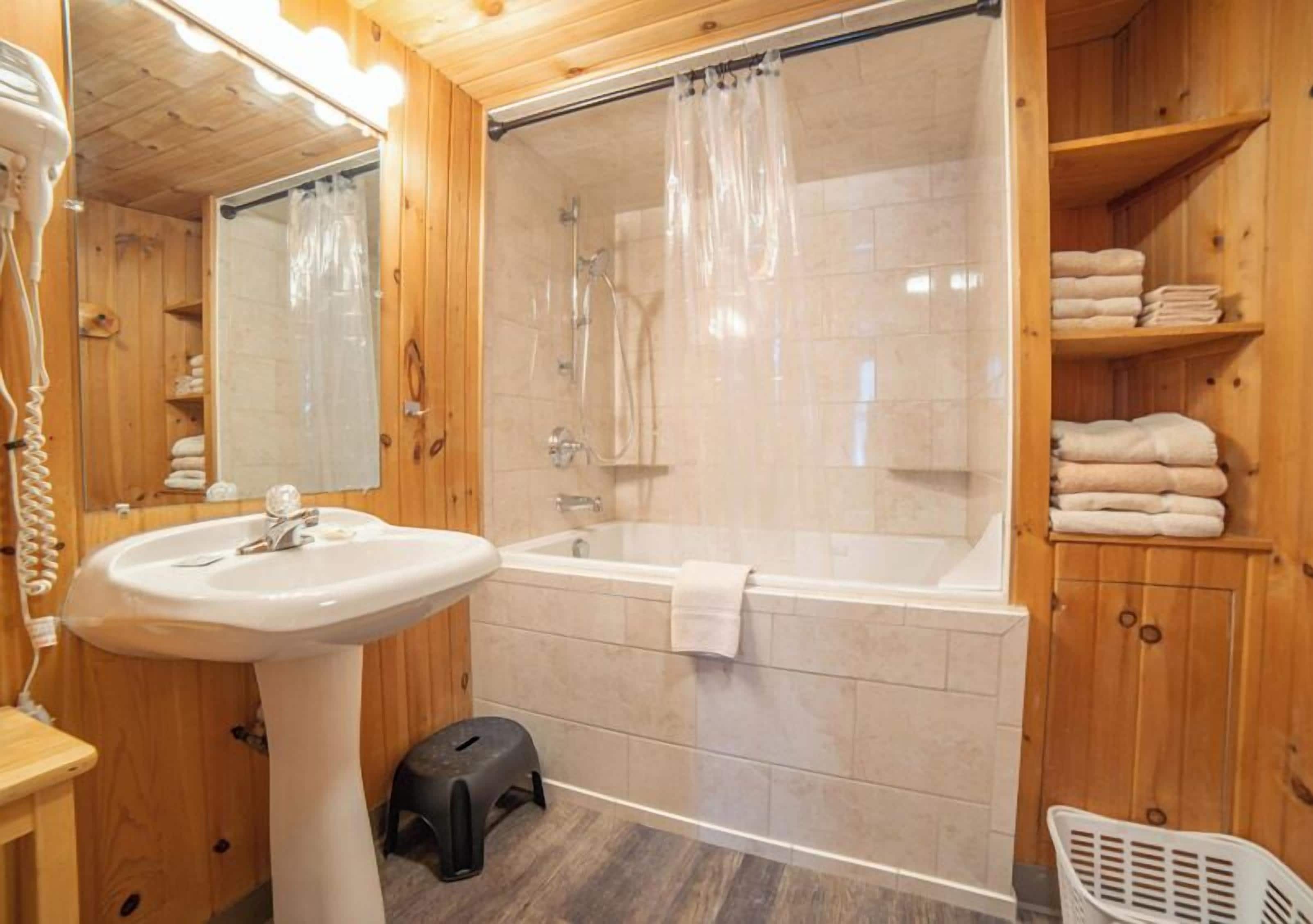 Baño de cabaña de madera con lavabo, bañera, ducha y repisas con toallas.