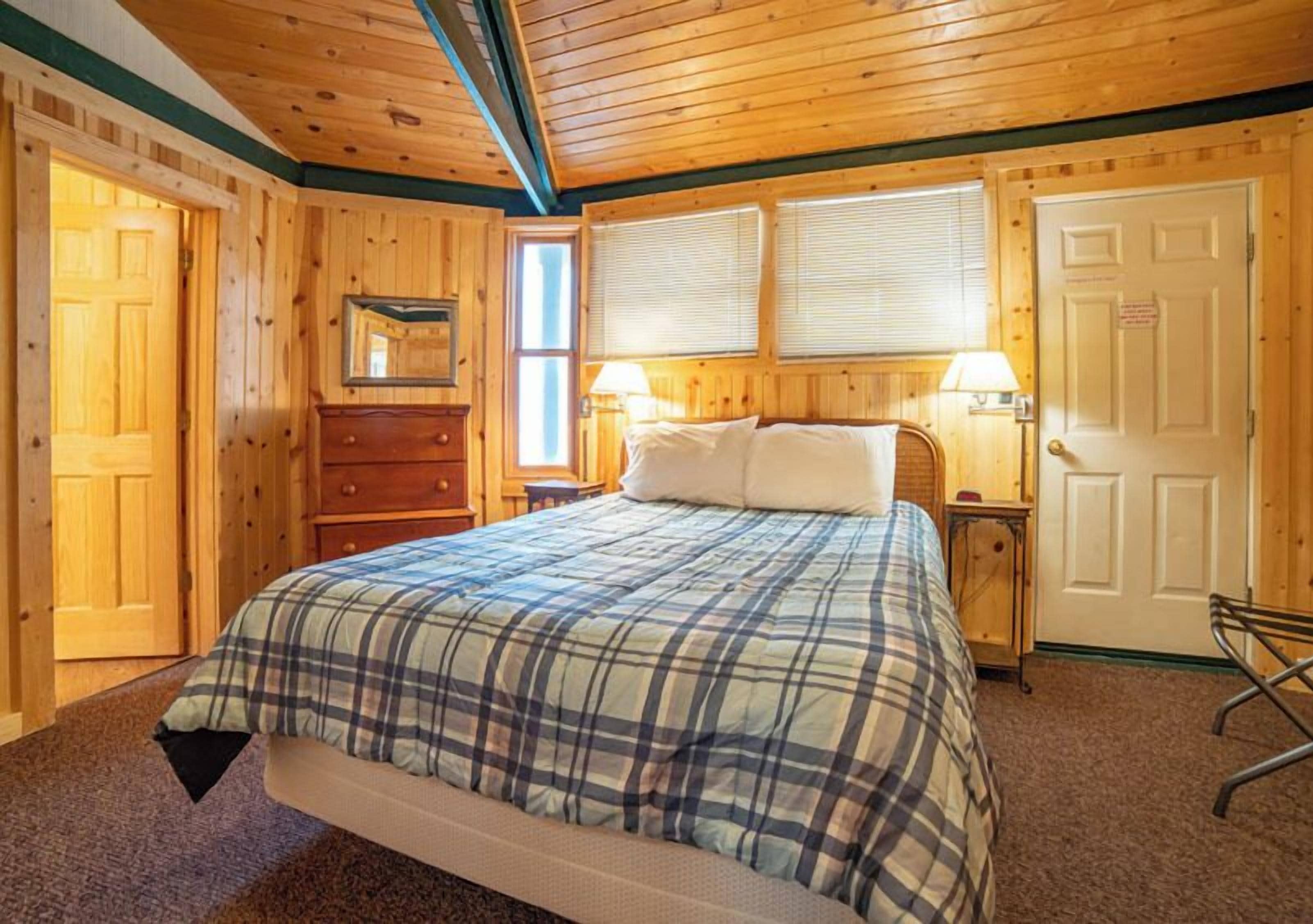 A wooden-paneled bedroom with a bed, dresser, bedside tables, and a door.