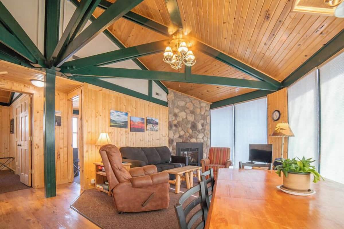 A cozy living room with a fireplace, wooden beams, and a stone wall.