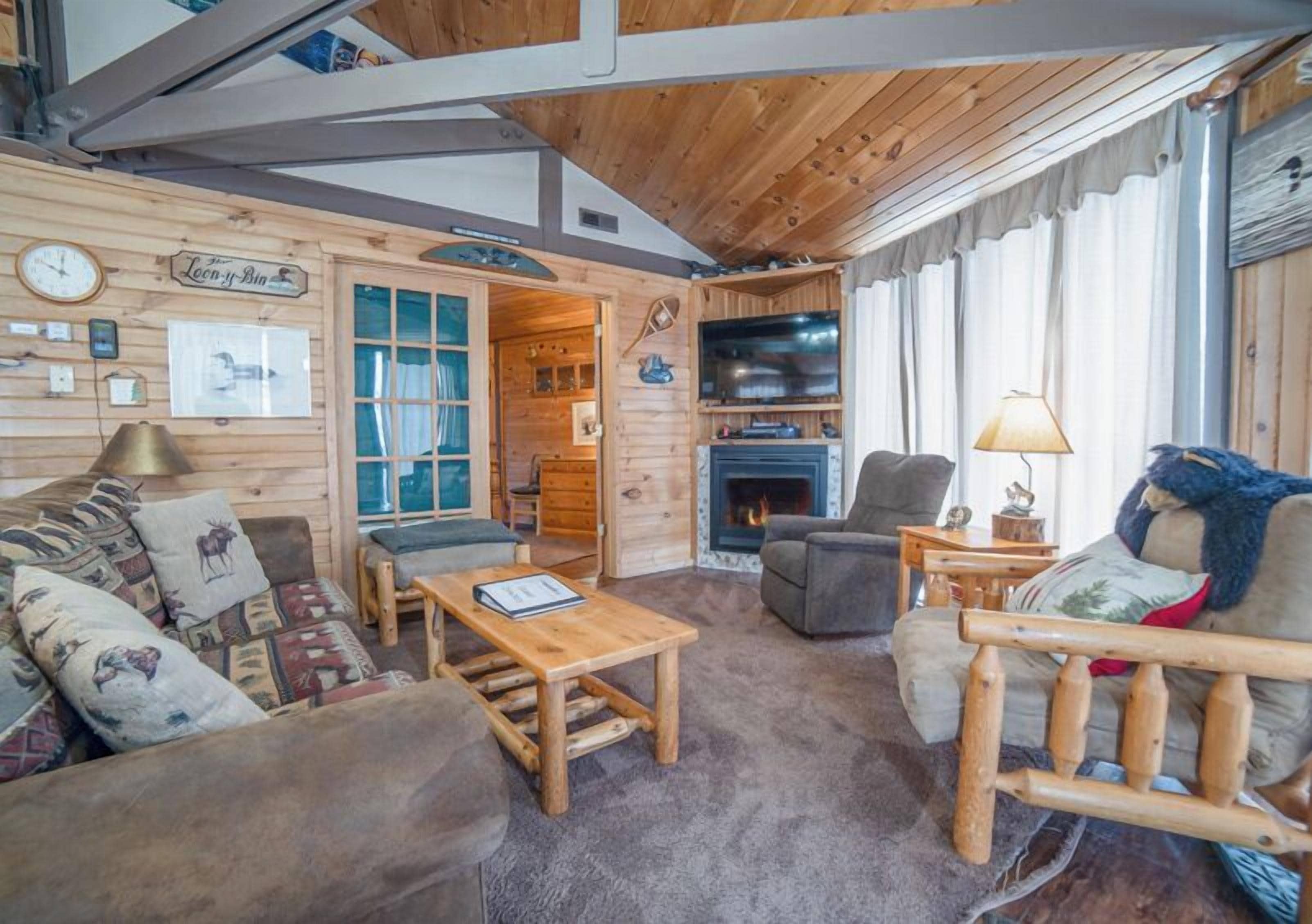 A cozy cabin interior with a fireplace, wooden furniture, and a television.