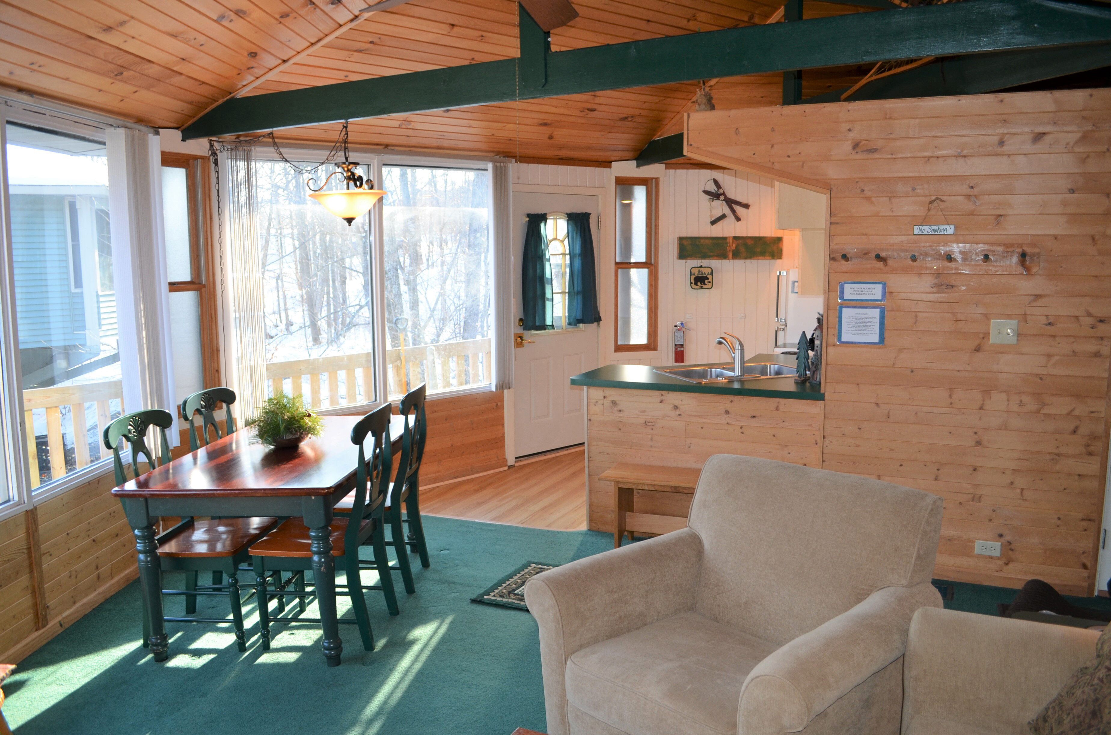 Interior de una cabaña de madera con comedor, cocina y una sala de estar acogedora.