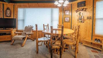 Un interior de madera acogedor con una mesa redonda de madera y sillas, un televisor y un cartel con la palabra 'WELCOME' en la pared.