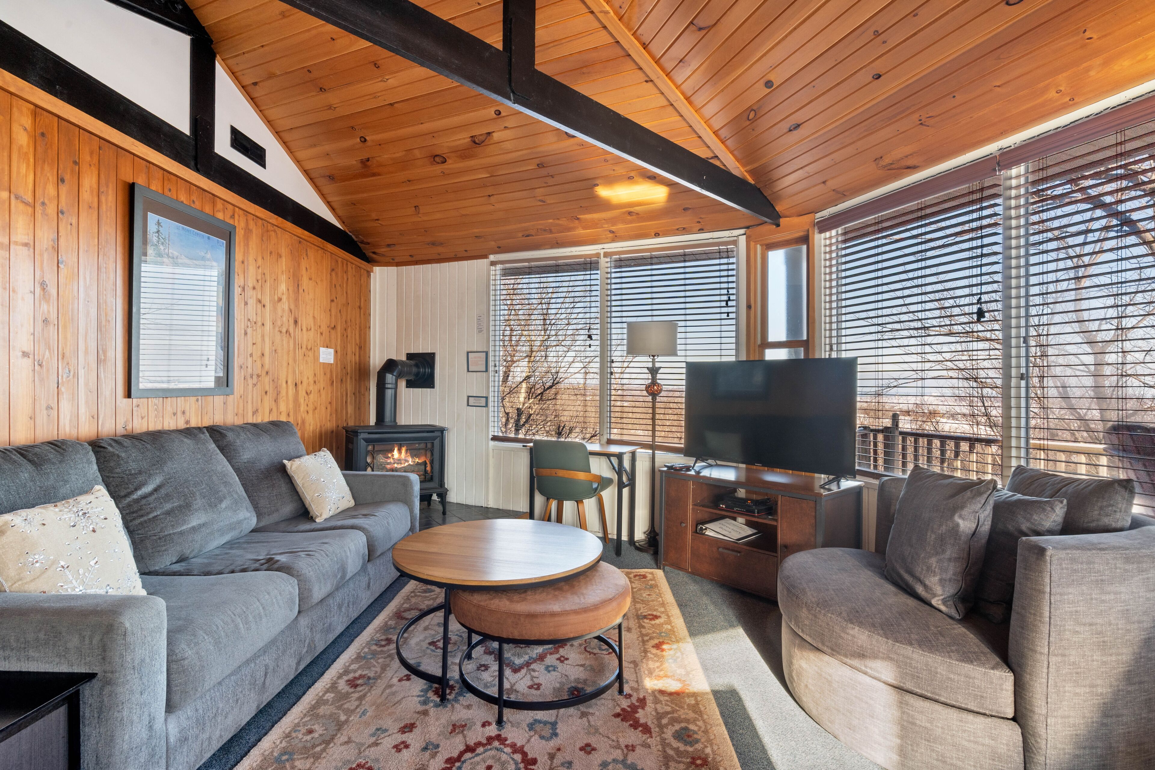 Un salón acogedor con chimenea, televisor y un ventanal con persianas.