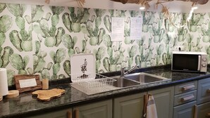 Una cocina con salpicadero decorado con motivos de cactus, utensilios de madera, un fregadero y un microondas.