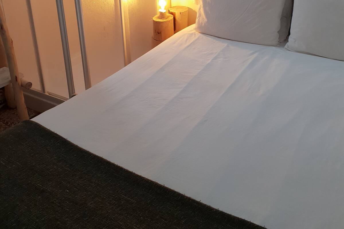 Een net opgemaakt bed met witte lakens, een houten hoofdbord en een bedlampje.