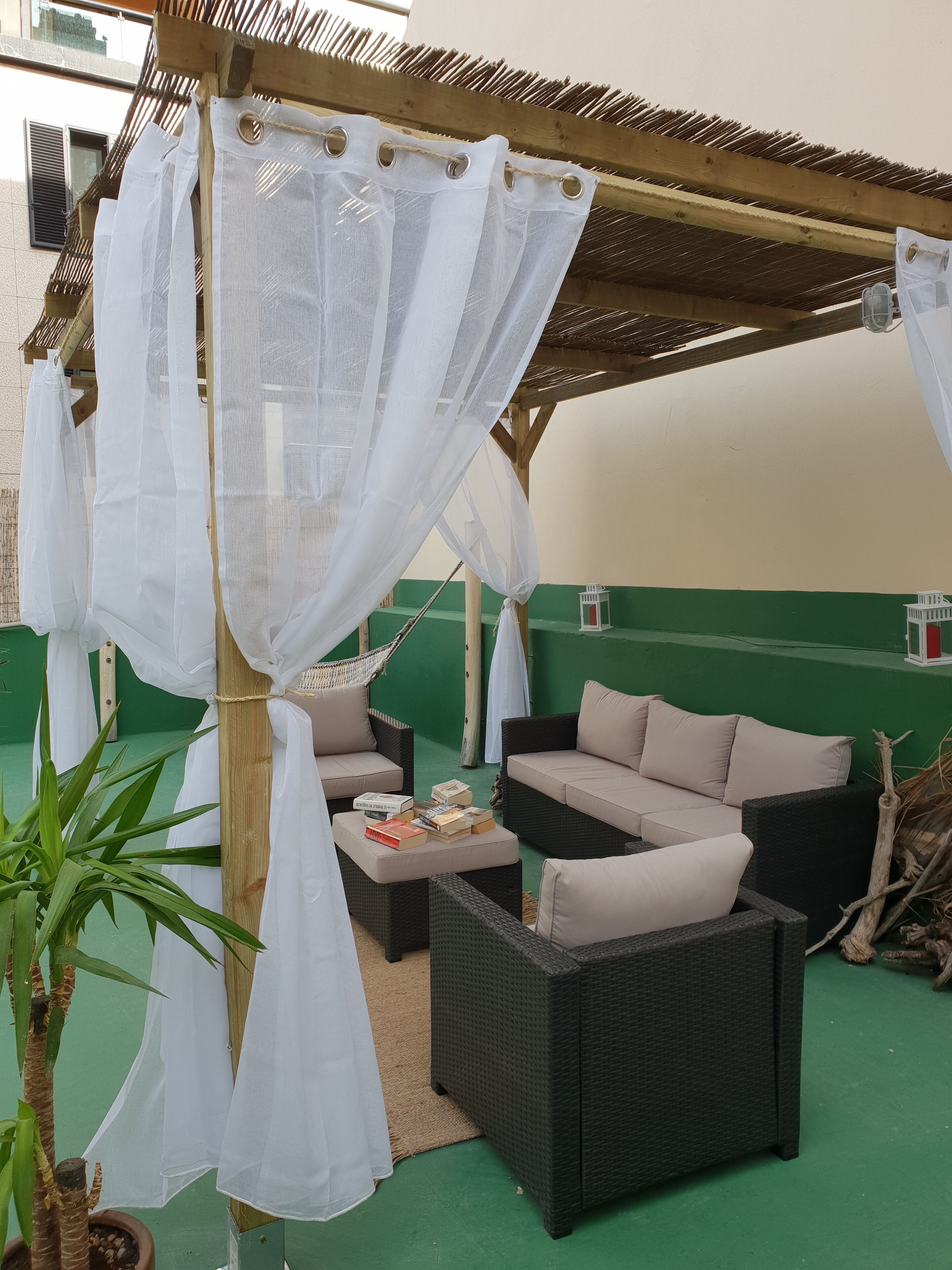 Un espacio de estar al aire libre con techo, mobiliario de mimbre y suelo verde.