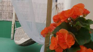 Una planta en maceta con flores anaranjadas, una silla colgante y un piso verde.
