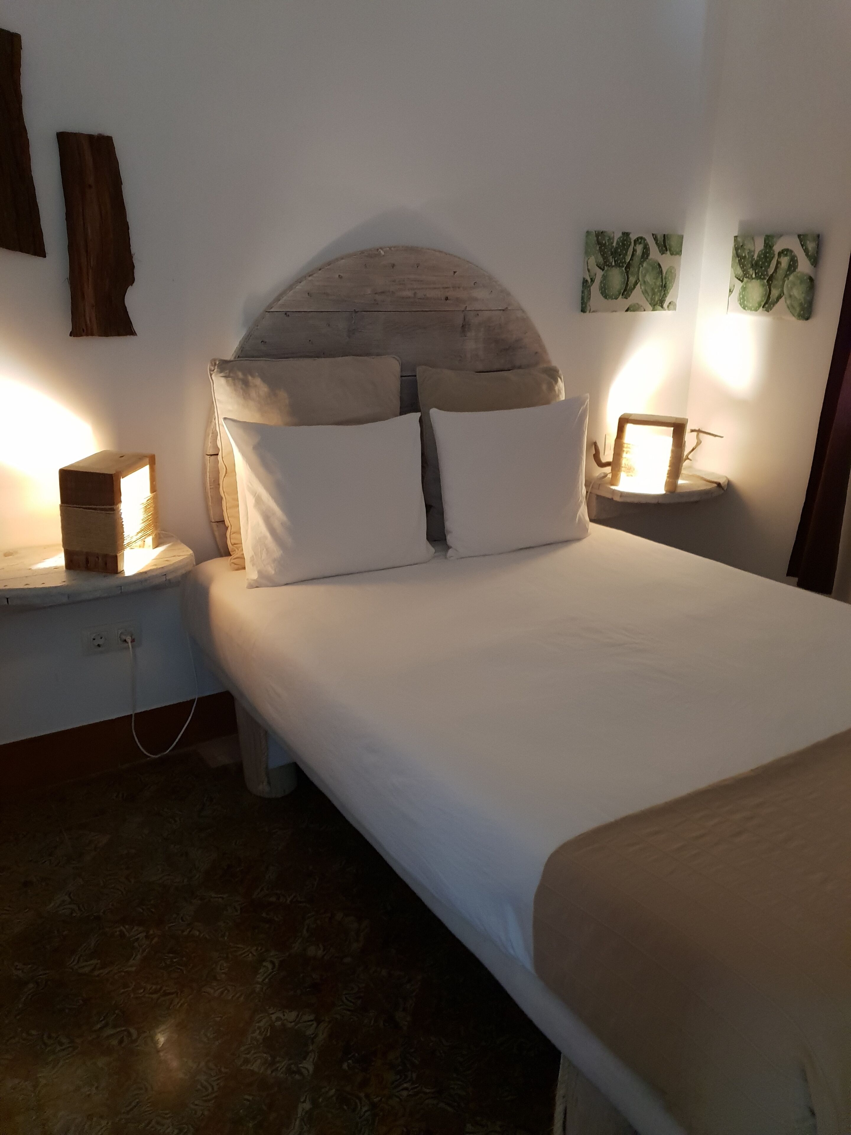 Una cama bien hecha con sábanas blancas y dos almohadas, un cabecero de madera y mesitas de noche con lámparas.