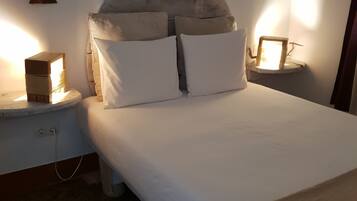 Una cama bien hecha con sábanas blancas y dos almohadas, un cabecero de madera y mesitas de noche con lámparas.