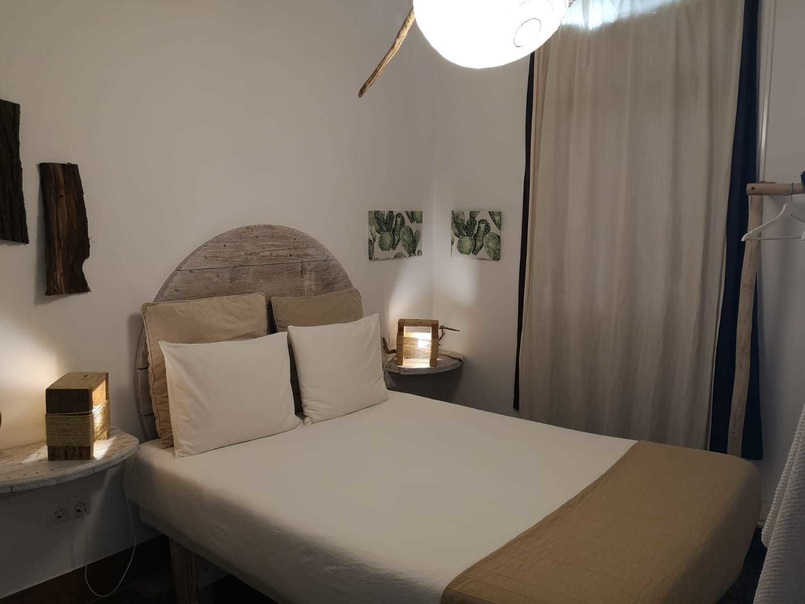 Un dormitorio ordenado con una cama grande, una mesita de noche con lámpara y una obra de arte en la pared.