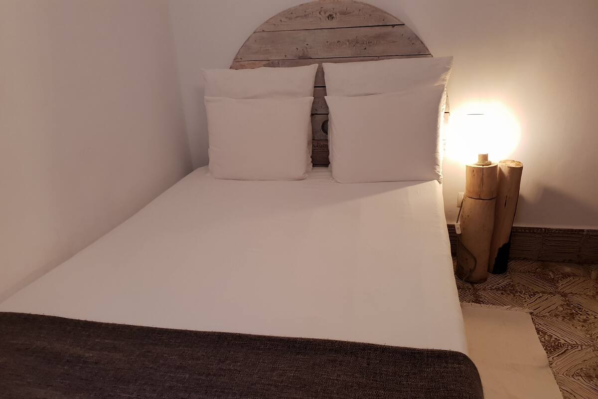 Een bed met witte lakens, een houten hoofdbord en een nachtkastje met een lamp.