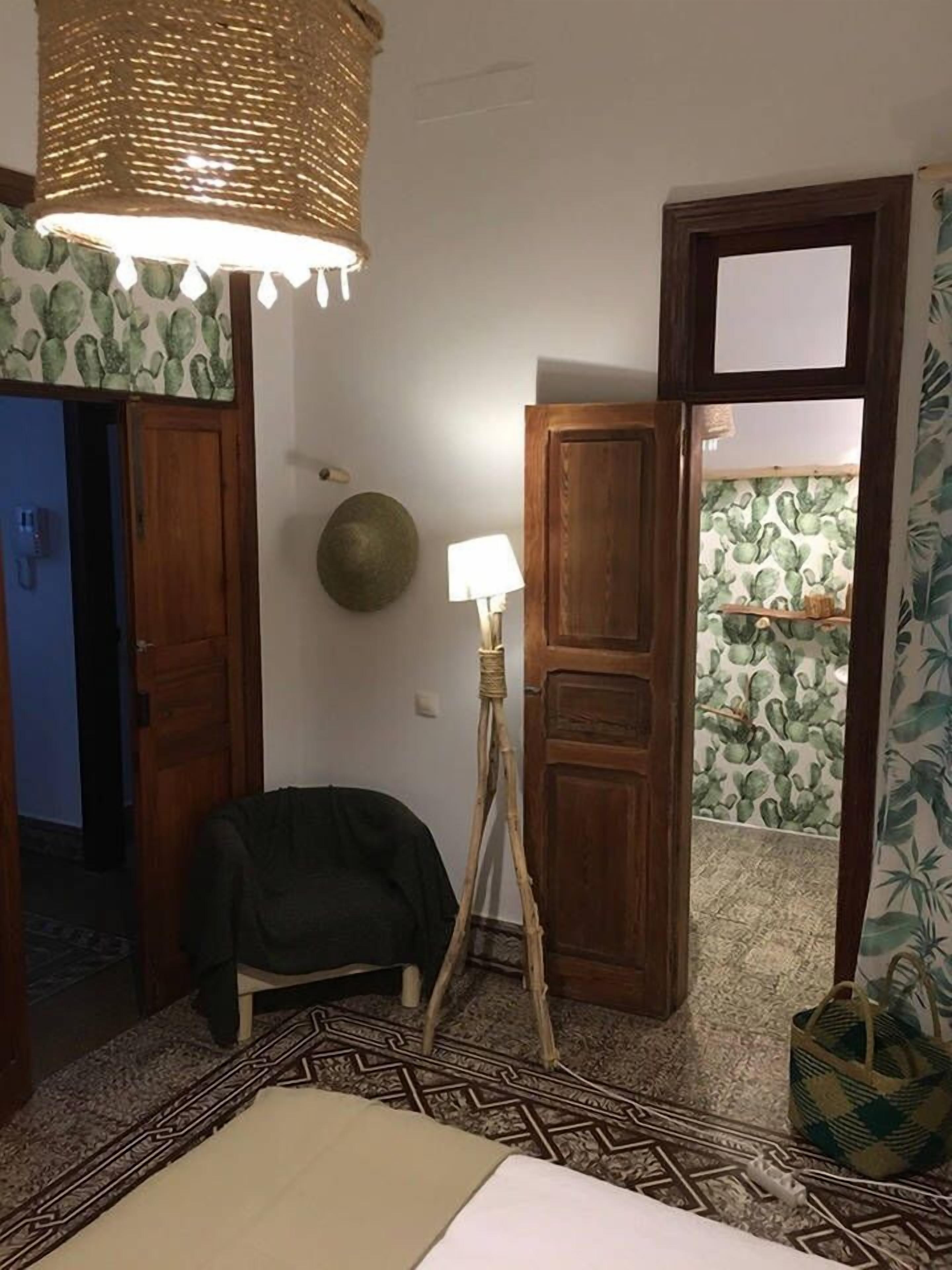 A room with a patterned carpet, a standing lamp, a wooden door, and a wall with a cactus print.