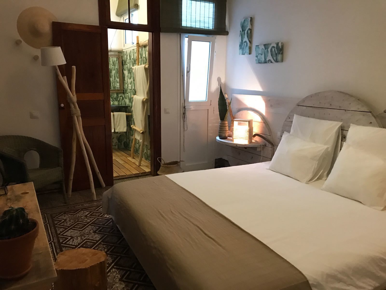 A bedroom with a large bed, a wooden ladder, a small table with a plant, and a window with a view of the outside.
