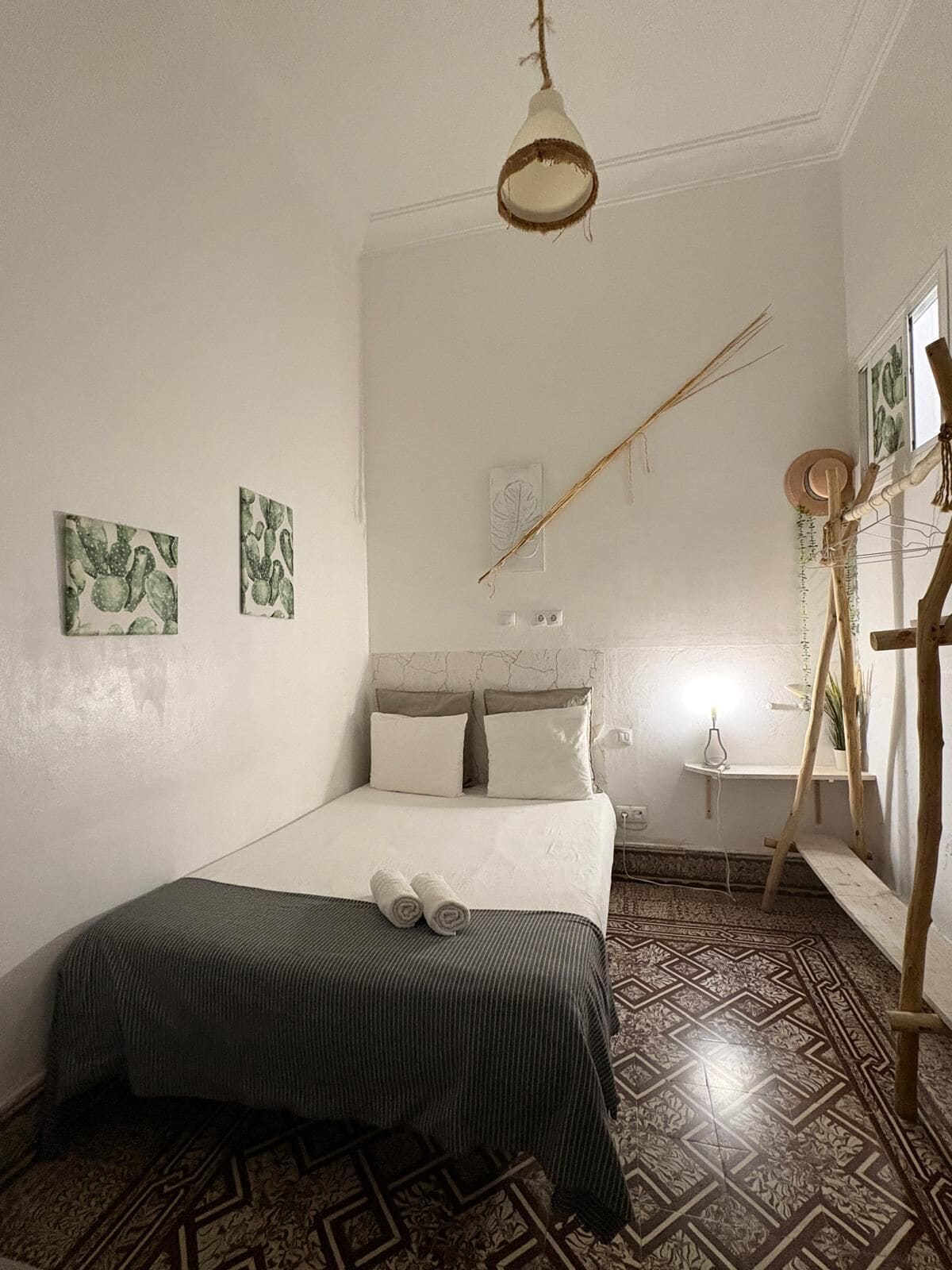 Habitació amb llit, llum penjant, escala de fusta i terres de rajoles amb dibuixos.