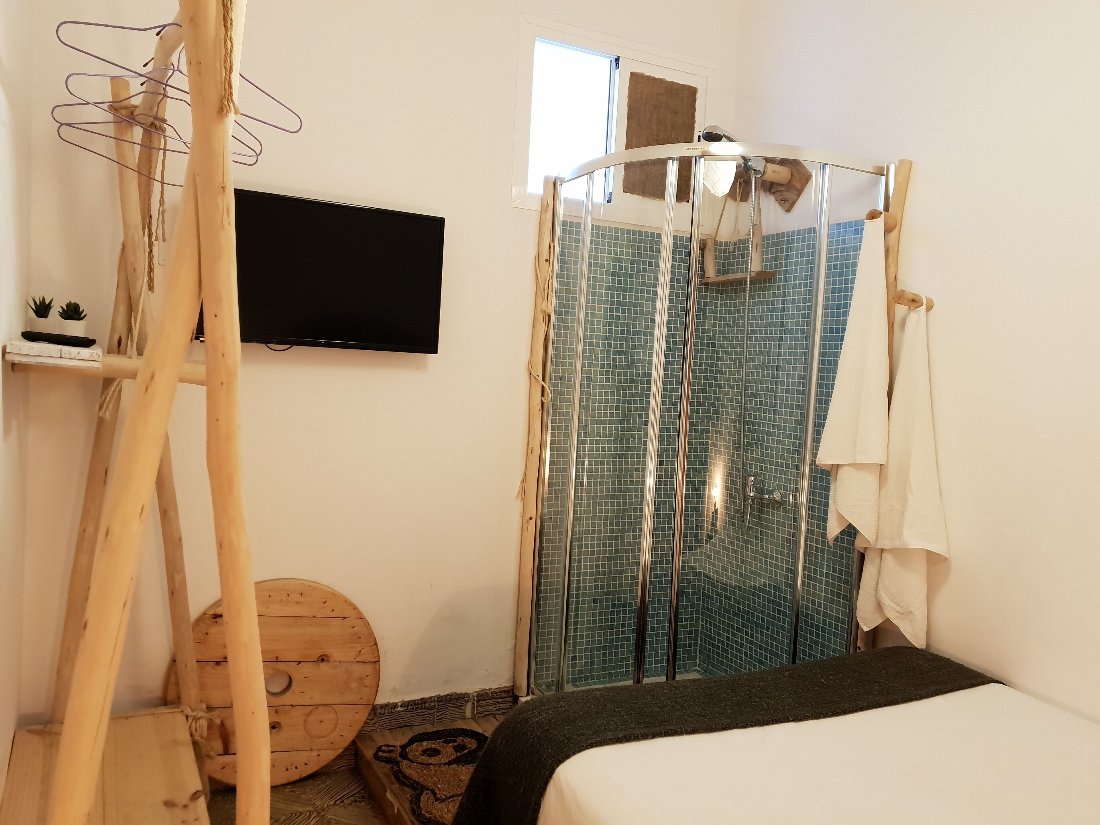 A bedroom with a bed, a wooden ladder, a television, a shower with blue tiles, and a small wooden stool.