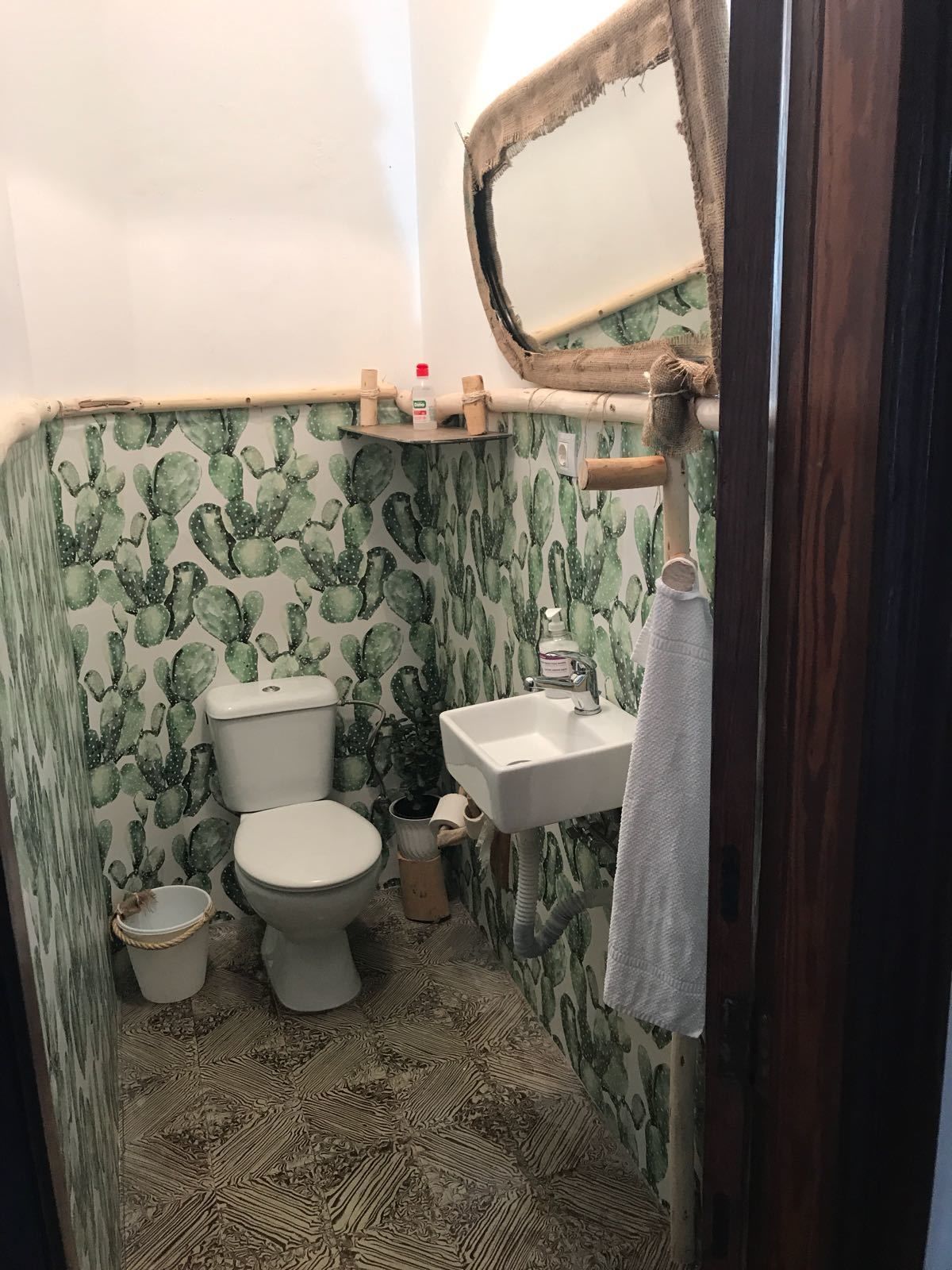 Un baño pequeño con papel tapiz con motivos de cactus, un inodoro, un lavabo y un espejo.